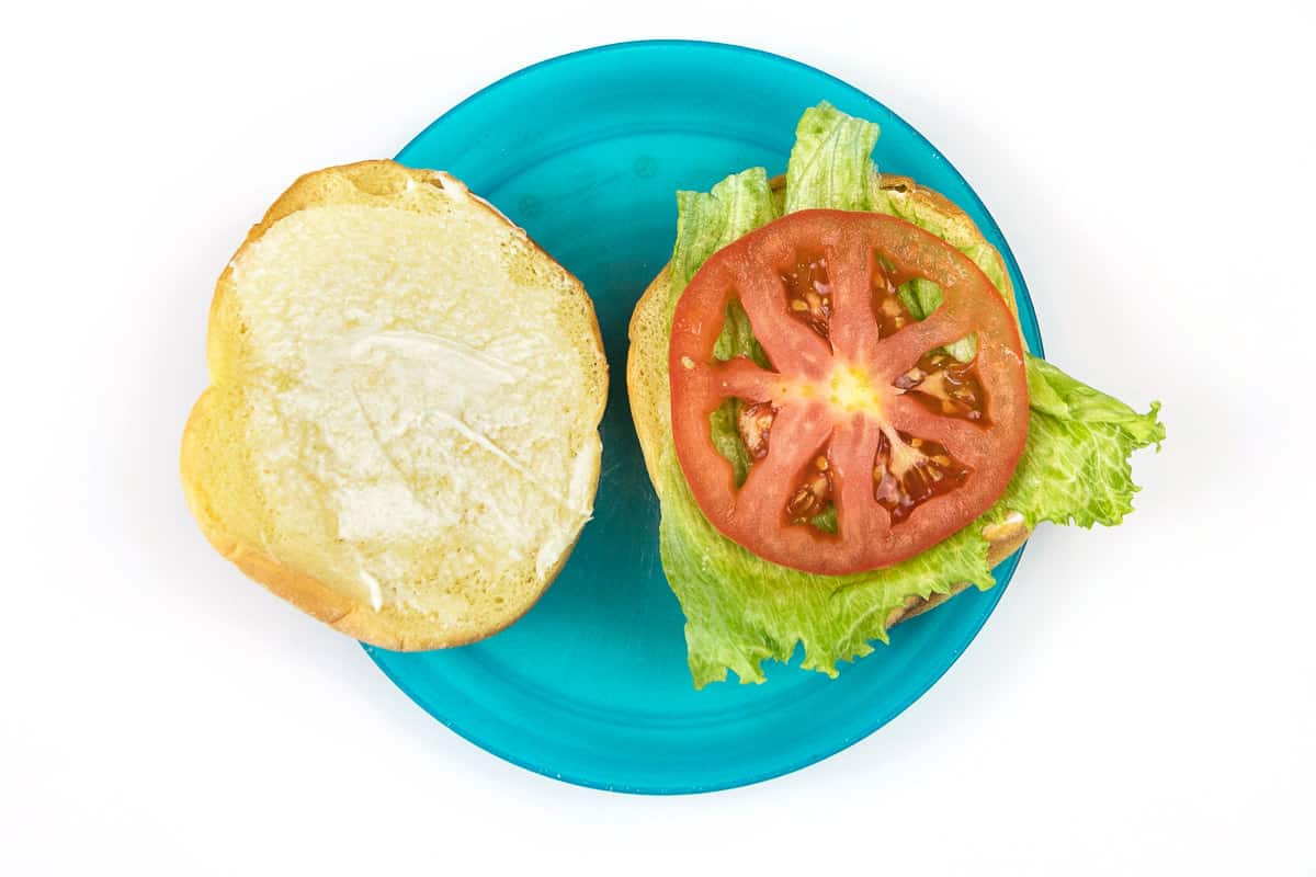 A hamburger bun with mayo, lettuce, and tomato on a plate.