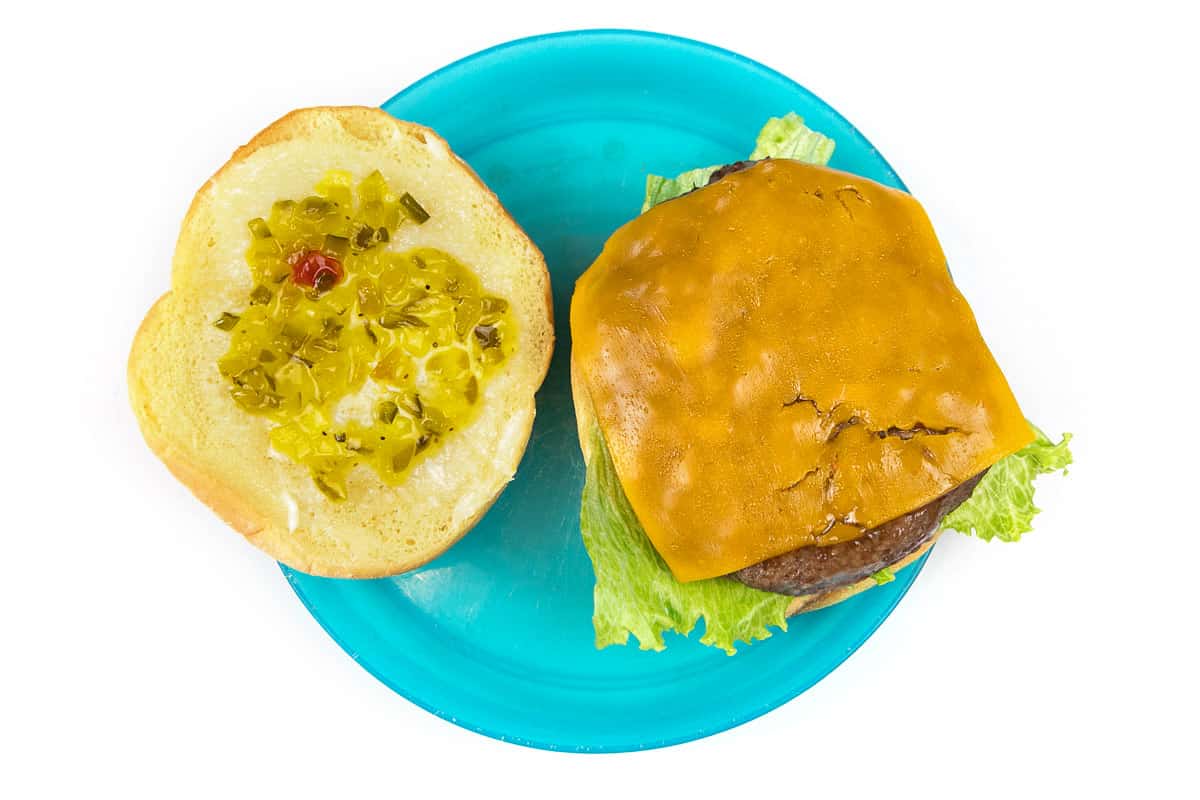 A hamburger patty with cheese, lettuce, tomato, mayo, and relish on a bun.