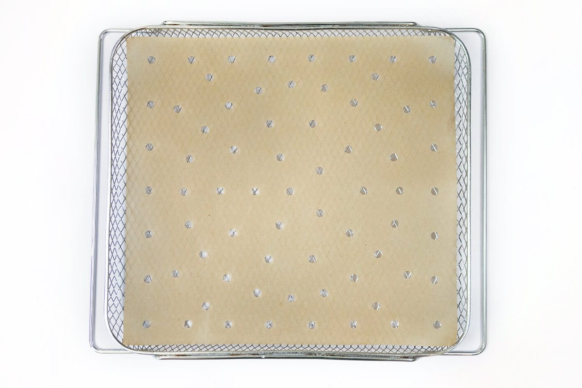 Parchment paper with holes is placed on the air fryer basket.