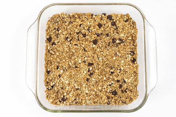 With the back of a spoon, press the granola bar mixture down into an eight by eight inch baking dish.