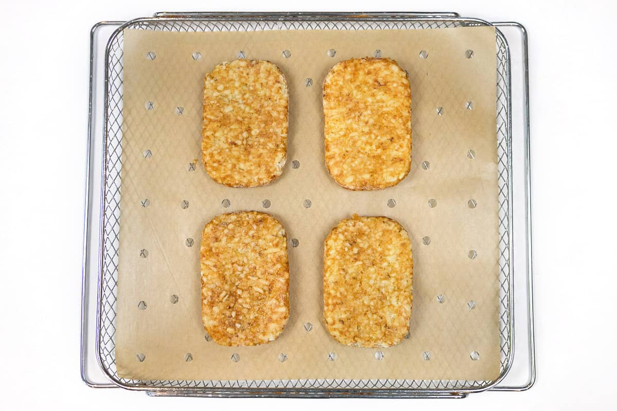 We laid parchment paper with holes in it on the air fryer basket, then put four frozen hash brown patties on top of the parchment paper.
