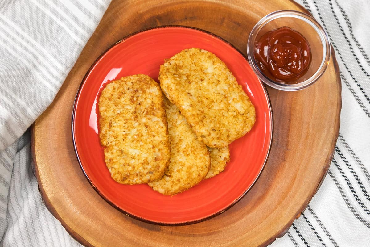 Four hash browns on a plate with ketchup as a dipping sauce.