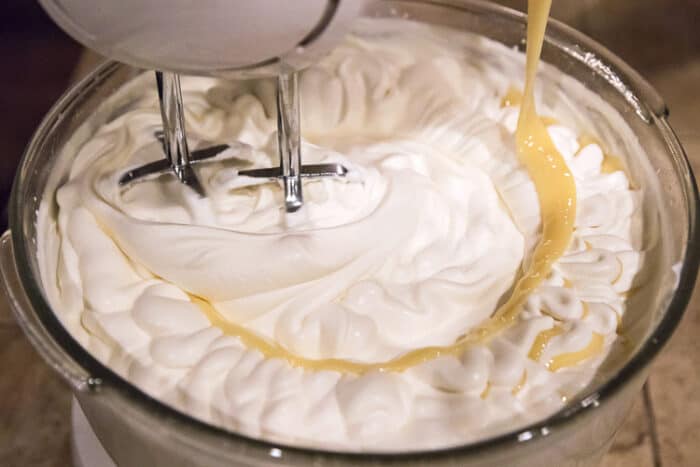 Two cans of condensed milk, each 14 ounces, is added to the whipping cream with the mixer on low speed.