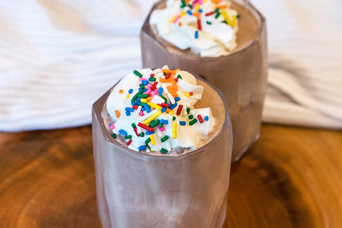 Finished product of the homemade chocolate milkshake topped with whipped cream and rainbow sprinkles.