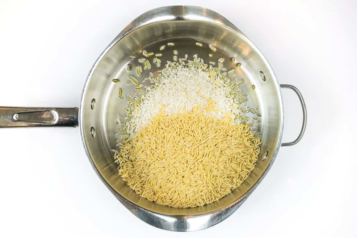 Olive oil, long-grain rice, and orzo pasta in a frying pan.