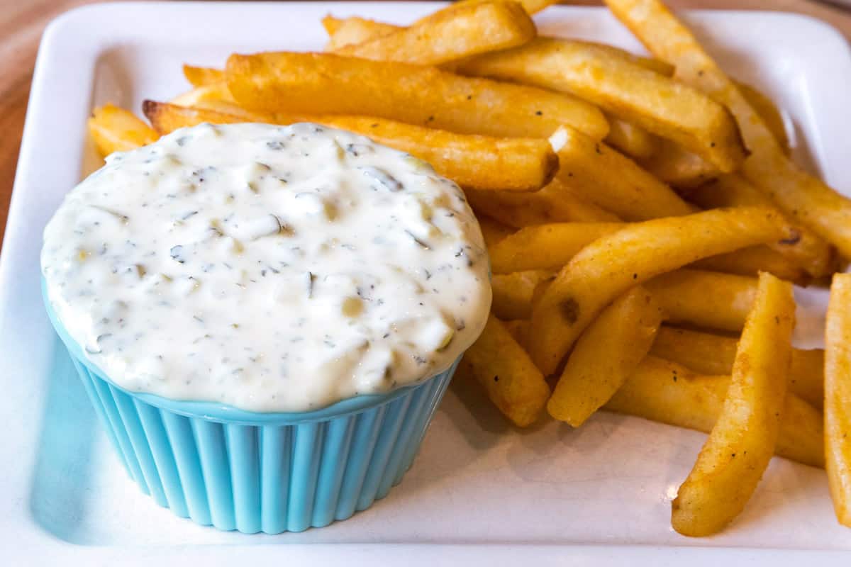 Tartar sauce in a bowl next to French fries on a plate.