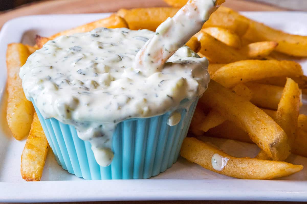 Homemade tartar sauce in a bowl with a plate of fries.