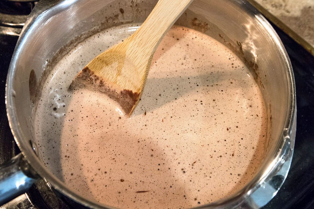 Hot water is added to the sweetened condensed milk, unsweetened cocoa powder, vanilla extract, and salt in the pot.