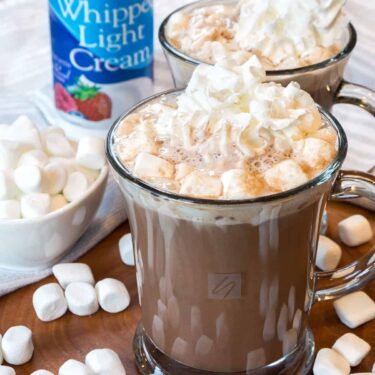 Close up of hot chocolate in a cup surrounded by marshmallows and whipped cream.