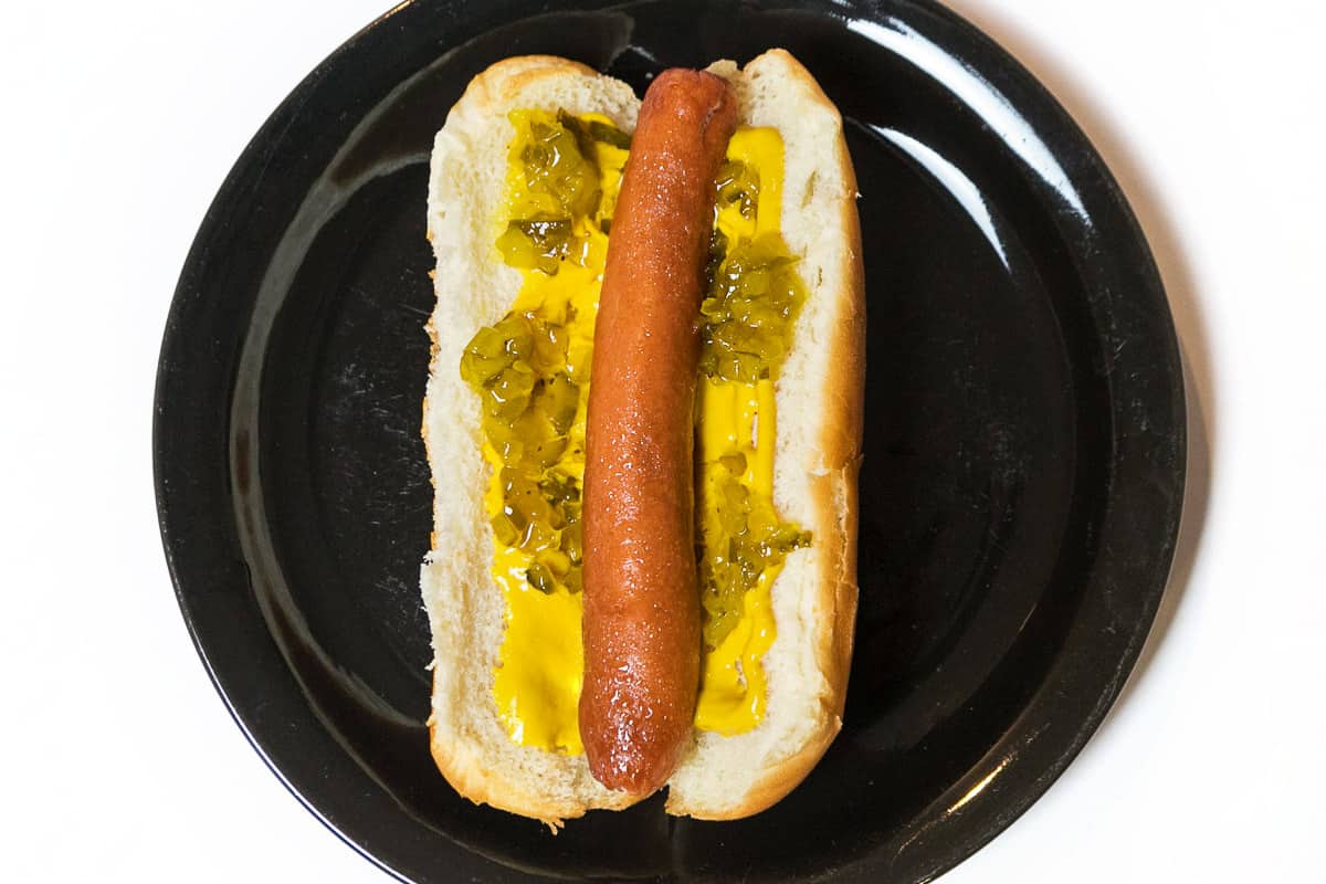 A cooked hot dog with mustard and relish on a plate.