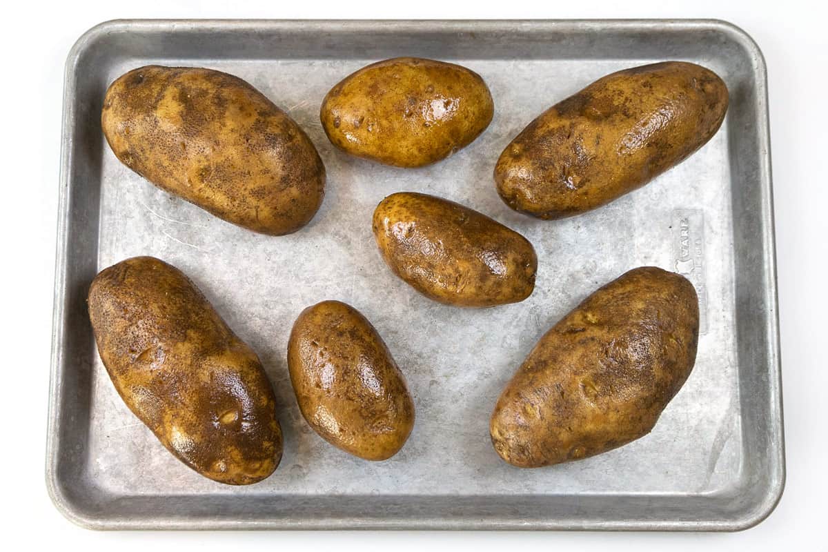 Seven raw potatoes on a sheet pan.