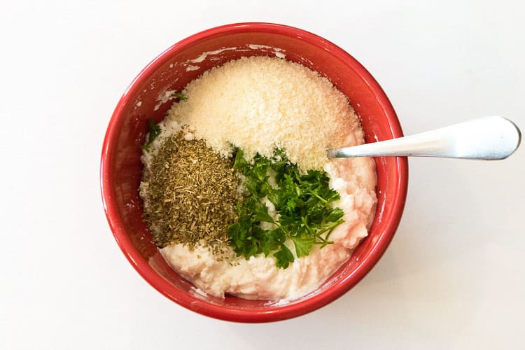 Ricotta cheese, Parmesan cheese, dried oregano leaves, and parsley in a bowl.
