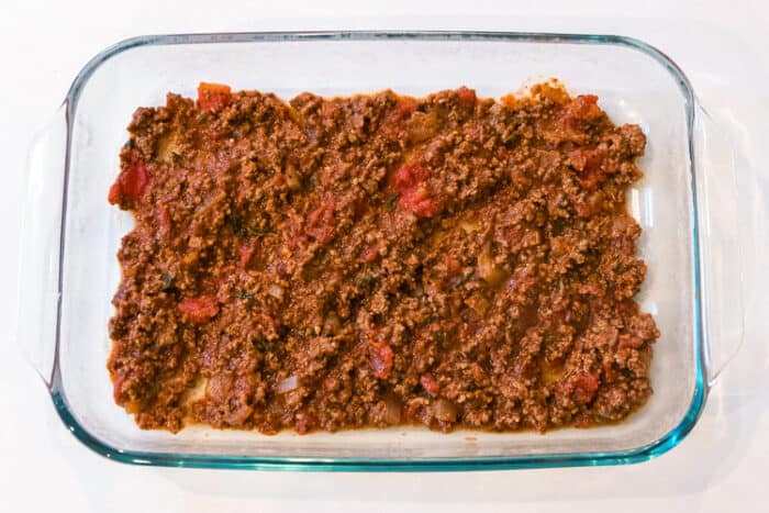 Baking pan with a layer of the ground beef mixture.