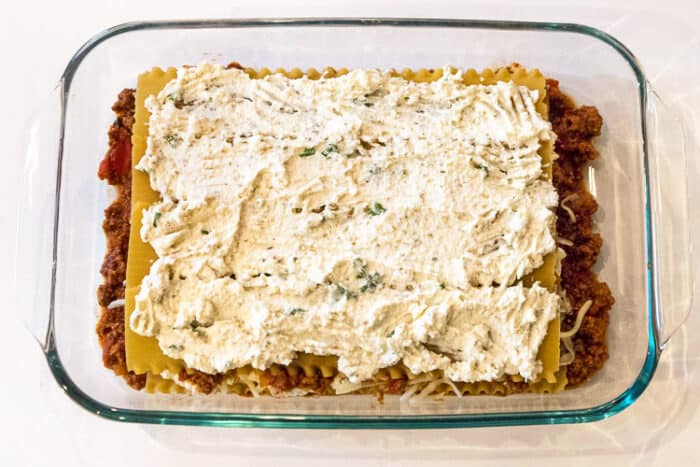 Another layer of the parmesan cheese, ricotta cheese, oregano, and basil  over the top of the lasagna noodles.