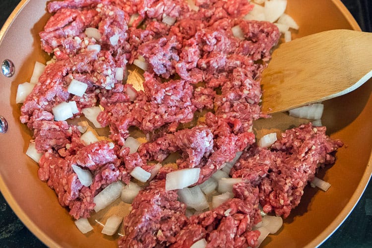Frying the lean ground beef, onions, and minced garlic in a frying pan until browned.