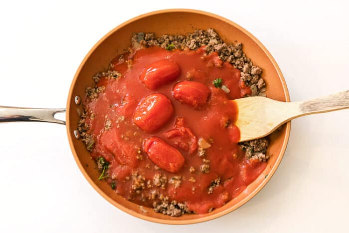 Whole tomatoes added to ground beef mixture.