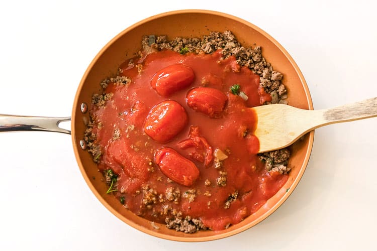 Whole tomatoes and tomato sauce are added to the ground beef mixture.