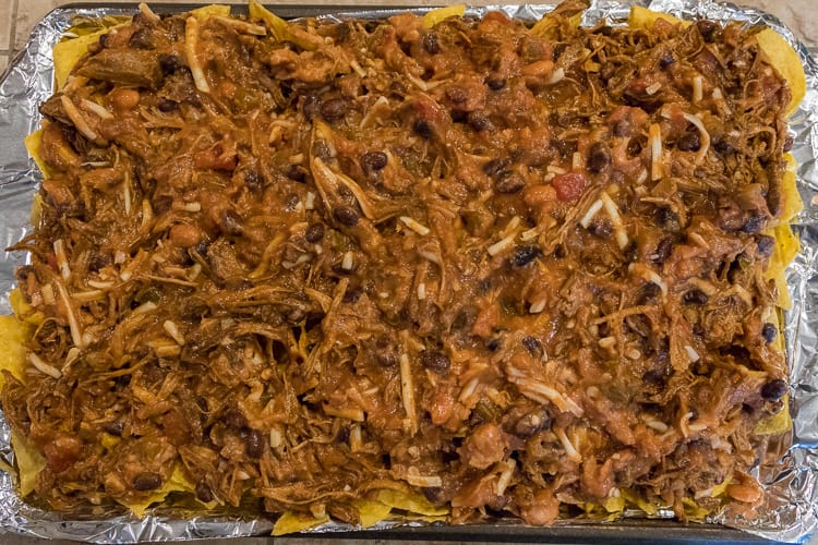 Spread the pulled pork mixture over the nacho chips on the sheet pan.