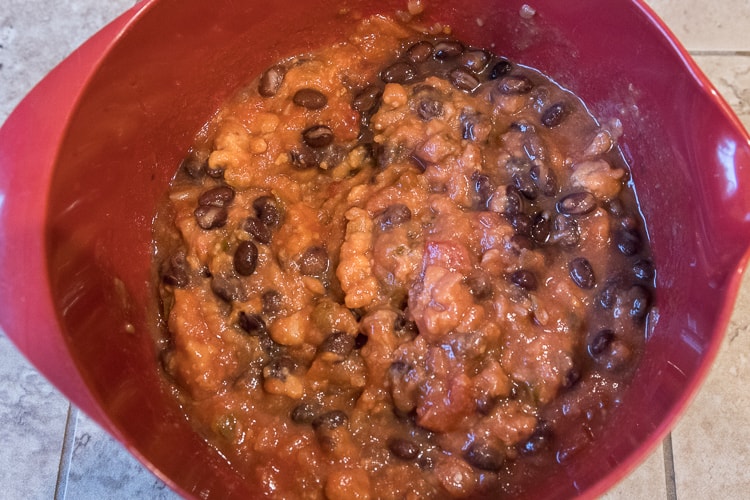 Black beans added to the medium-hot thick and chunky salsa and a can of refried beans in a bowl.