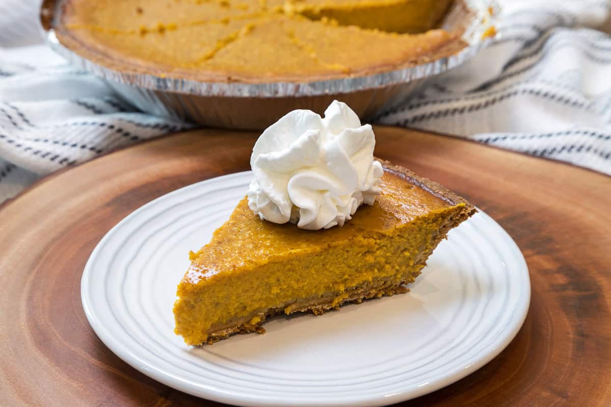 Pumpkin pie with Cool Whip on a plate.