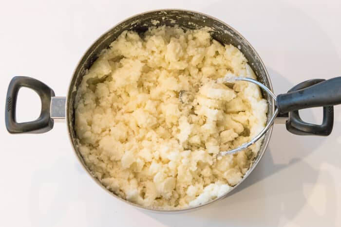 Potatoes getting mashed in a pot.