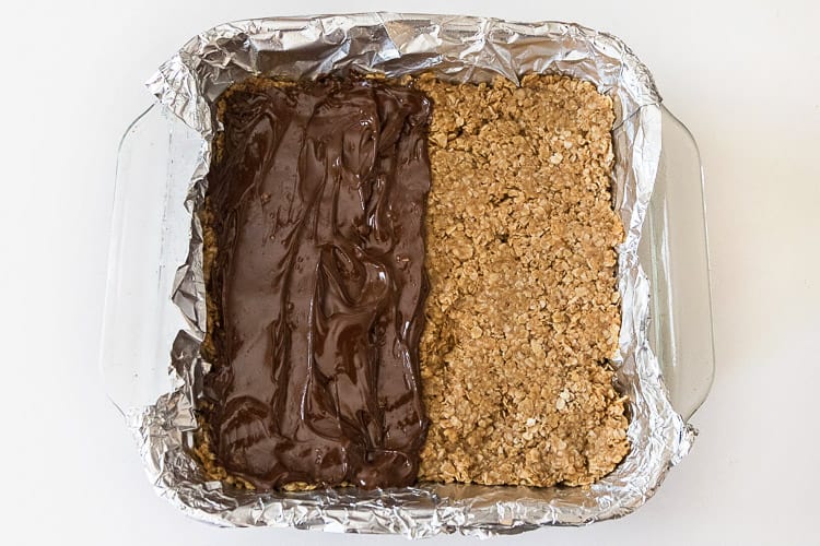 The melted chocolate chips are spread on half of the peanut butter bars.