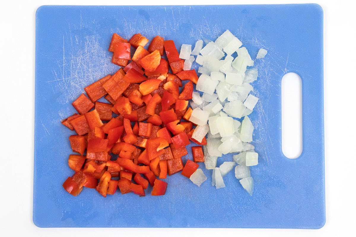One diced red bell pepper and one-half cup of diced onion on a cutting board.