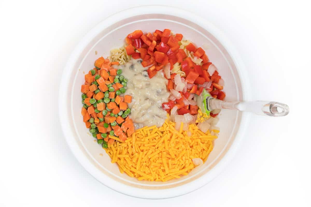 The diced red bell peppers, onions, cream of mushroom soup, peas, carrots, cheese, and milk are added to the tuna and egg noodles.