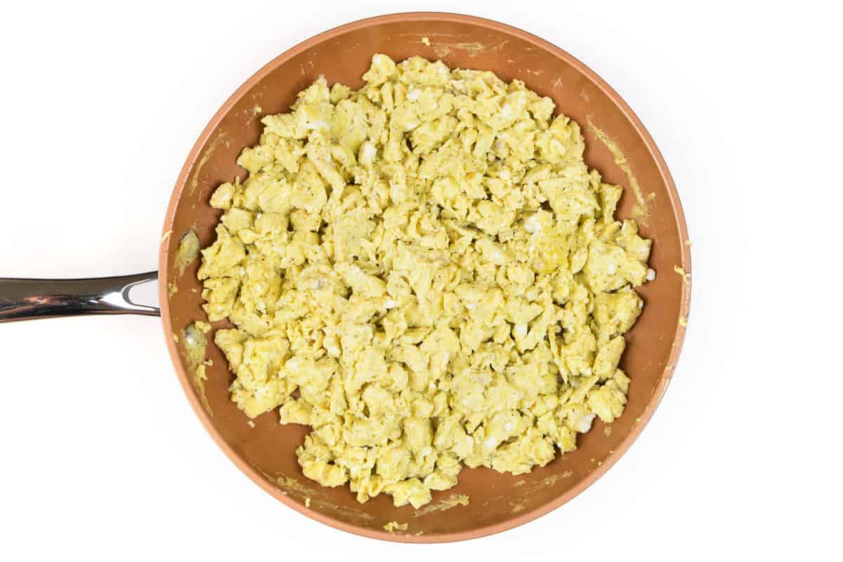 Eight scrambled eggs in a frying pan cooking.