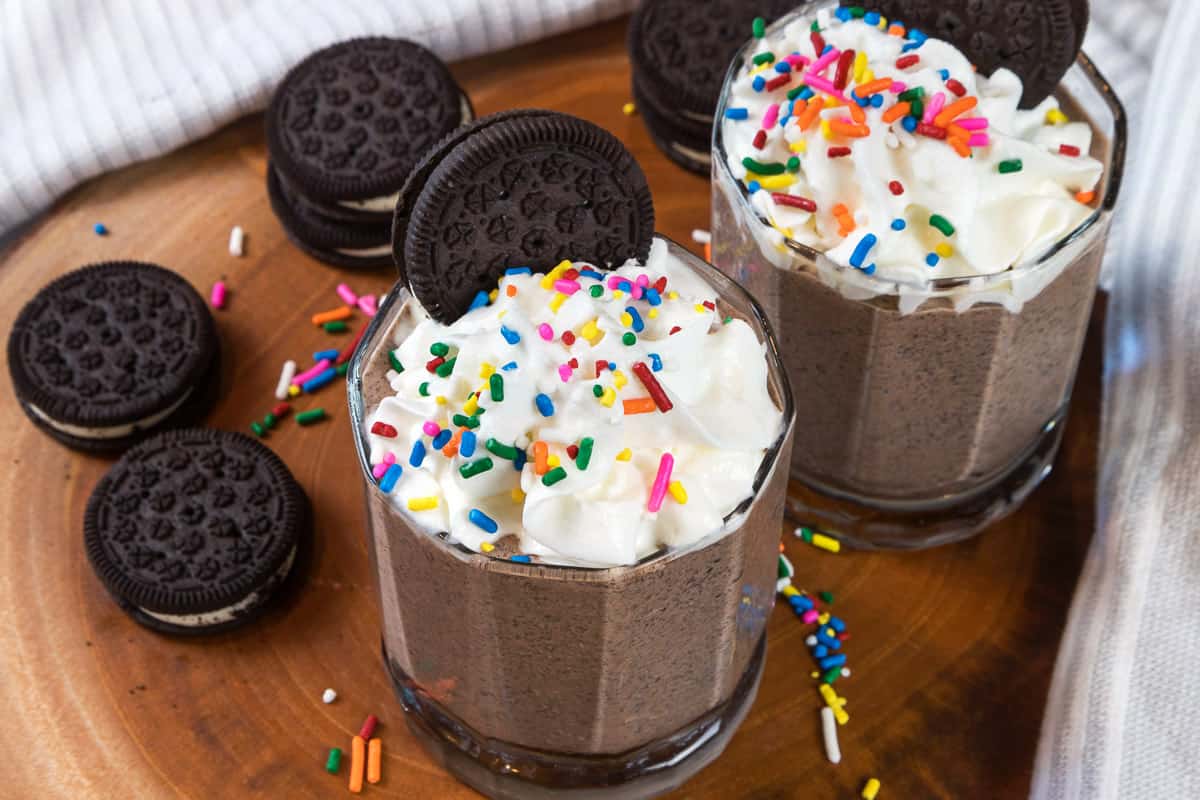 Two Oreo chocolate milkshakes with whipped cream and sprinkles.