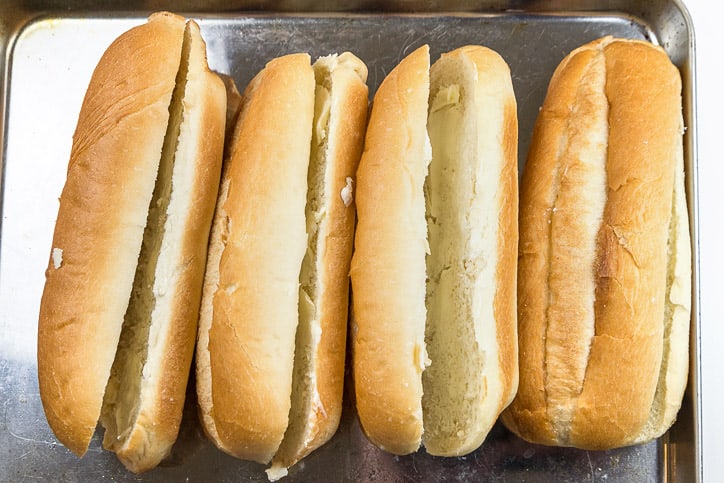Four soft buttered hoagie rolls on a toaster oven pan.