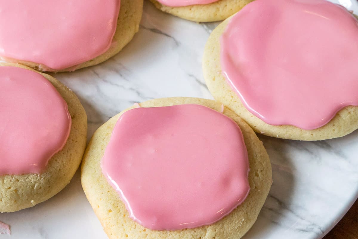 Sugar cookies on a plate with pink powdered sugar icing on them.