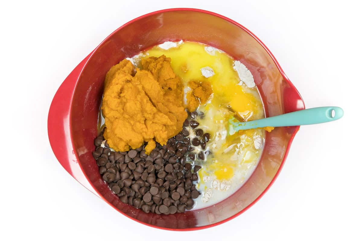 Melted butter, milk chocolate chips, pumpkin pie spice, pure pumpkin purée, milk, large eggs, and flour mixture in a bowl.