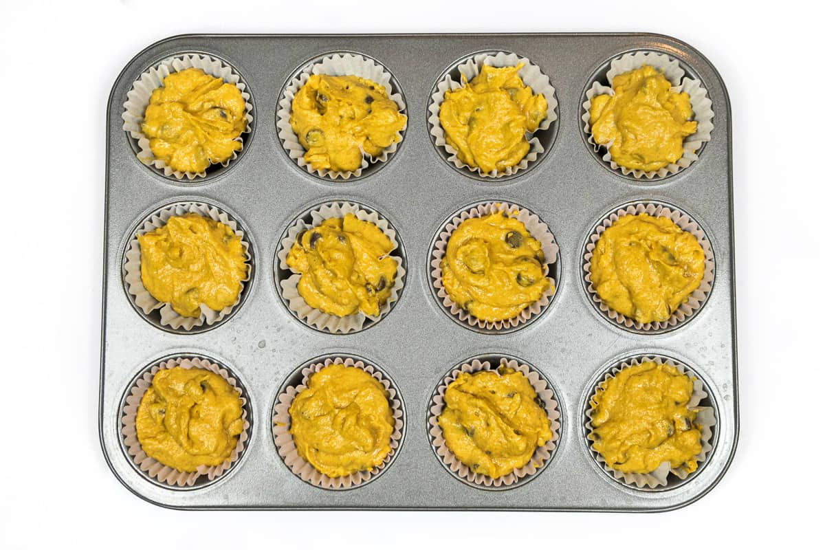 Twelve muffin cups filled with pumpkin chocolate chip batter.