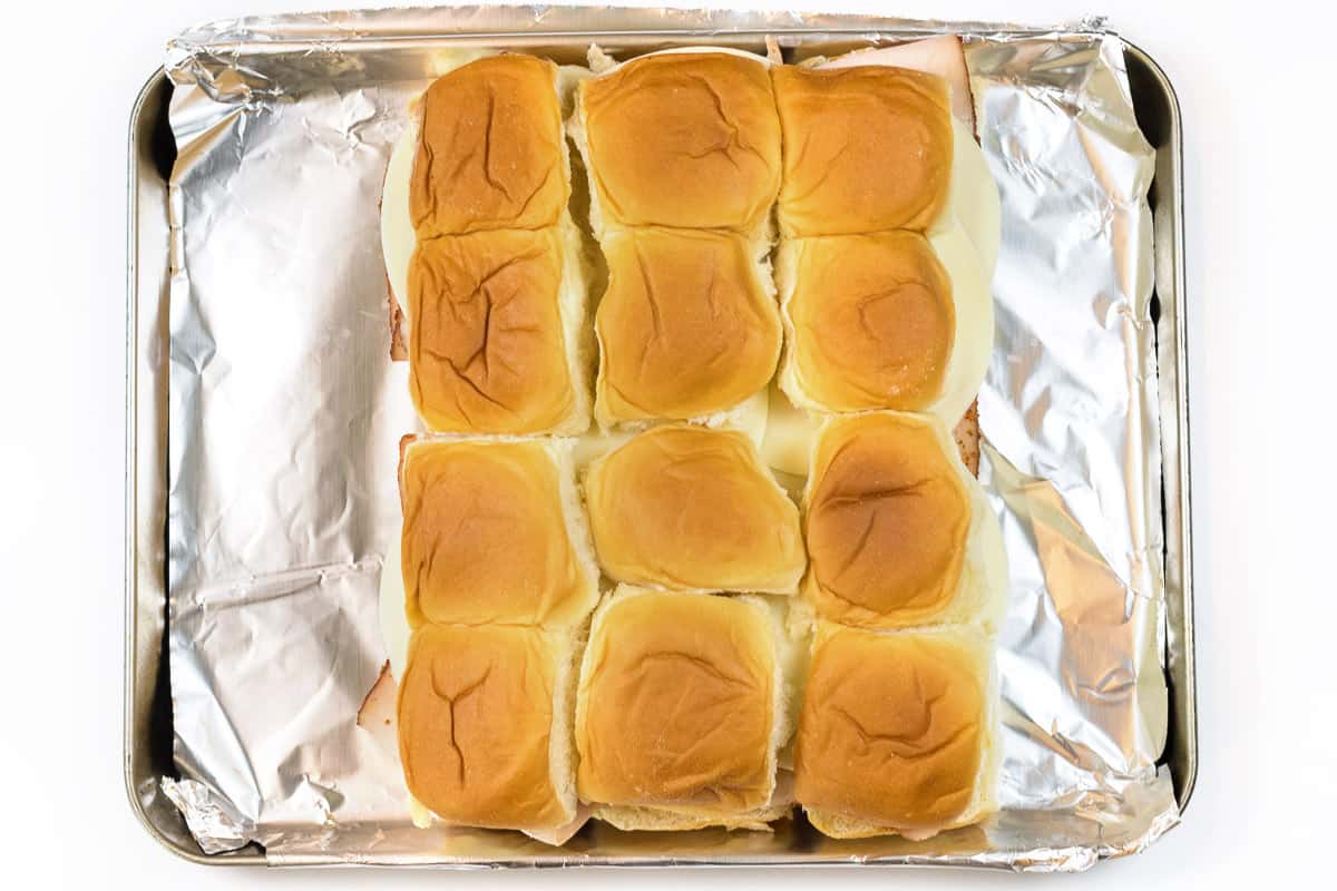 The tops of the Hawaiian rolls are put over the top of the provolone cheese.