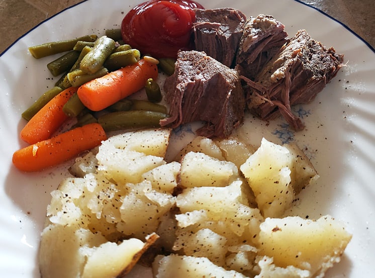 Pot roast on a plate with carrots, green beans, and potatoes.