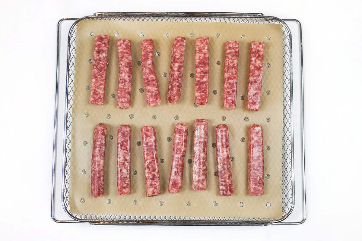 Parchment paper and sausage links on the air fryer basket.