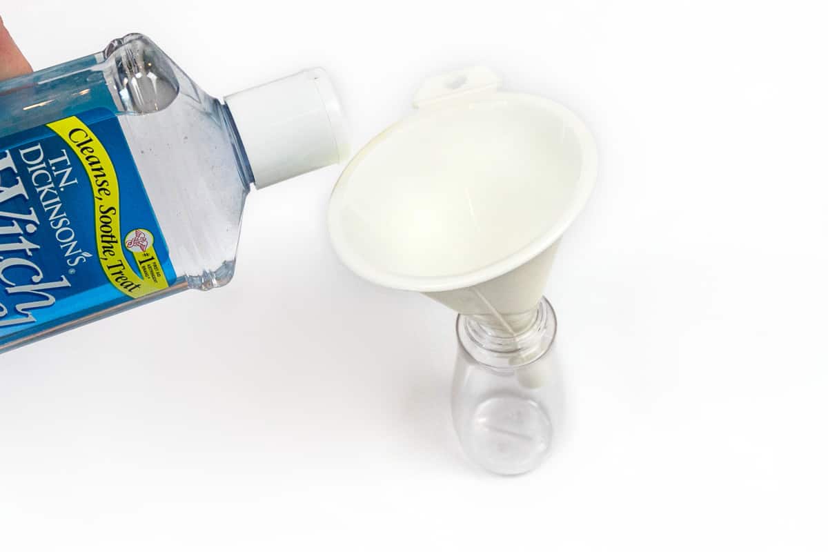 Filling a one-hundred milliliter spray bottle with fifty milliliters of witch hazel.