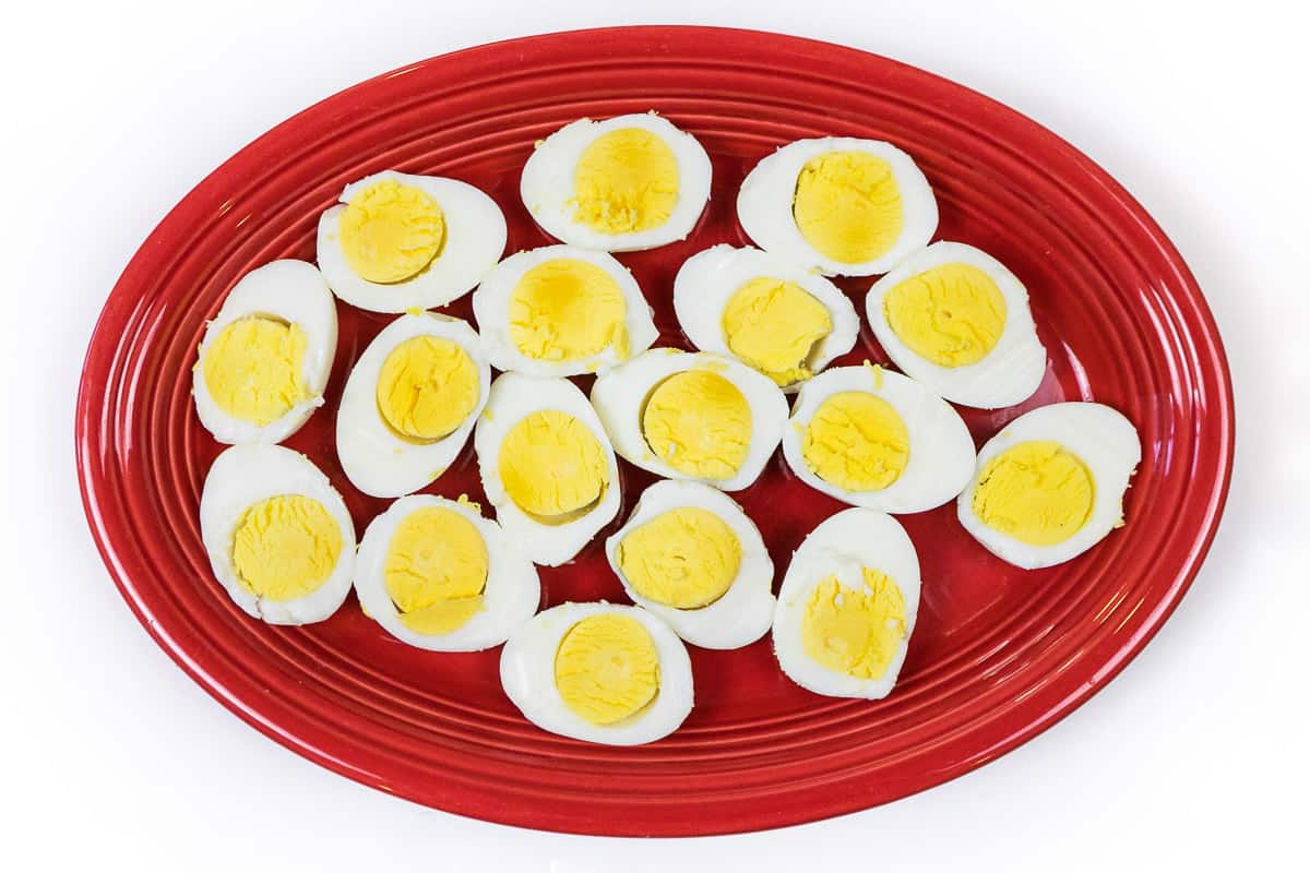 One dozen hard-boiled eggs cut in half lengthwise on a plate.