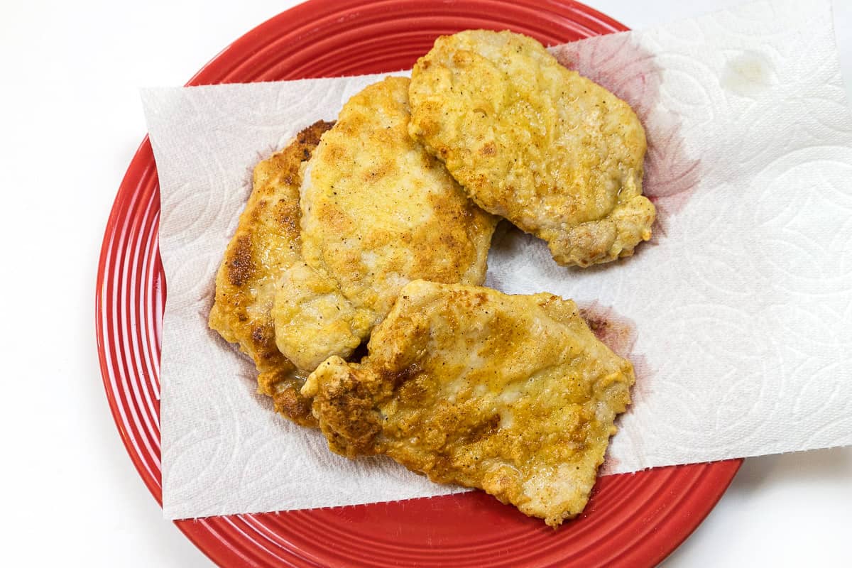 Fried Pork Chops Recipe on paper towels on a plate.