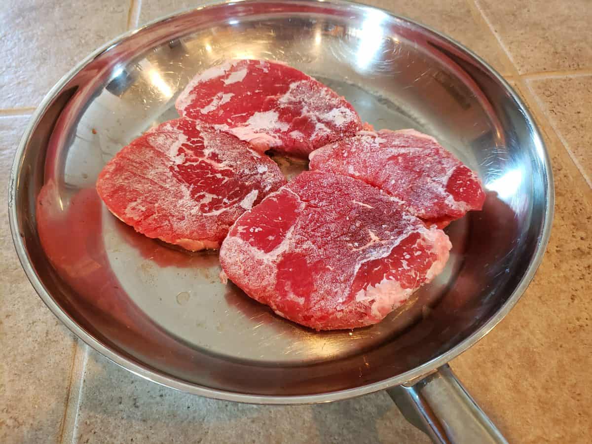 Four beef eye of round steaks in the frying pan with one tablespoon of cooking oil.