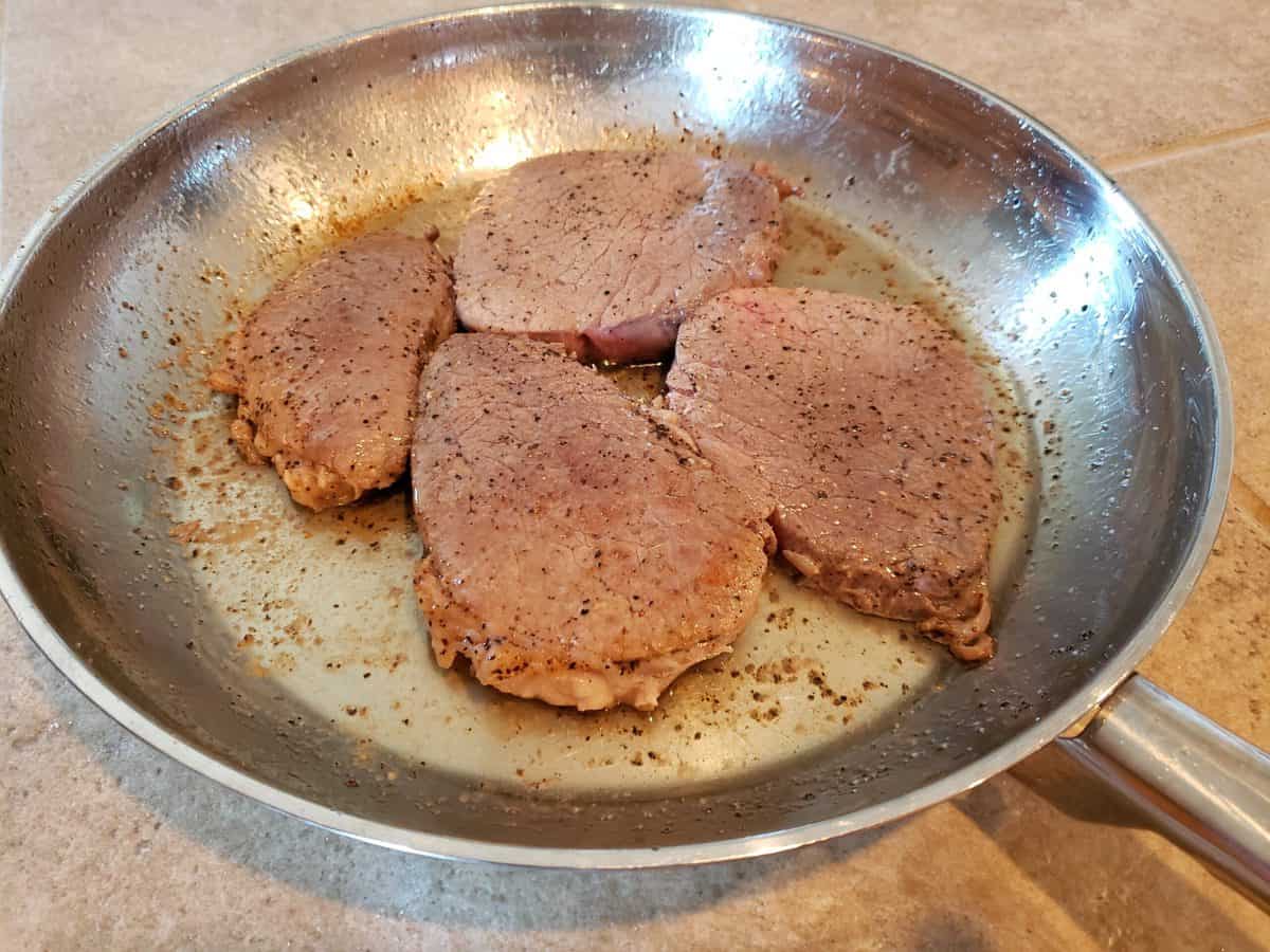 Four eye of round steaks are browning in the frying pan.