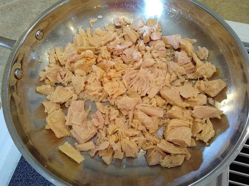 Olive oil and premium canned chicken in a frying pan.