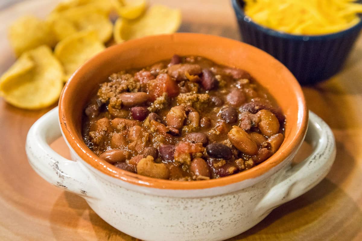 Chili in bowl with chips and cheese.