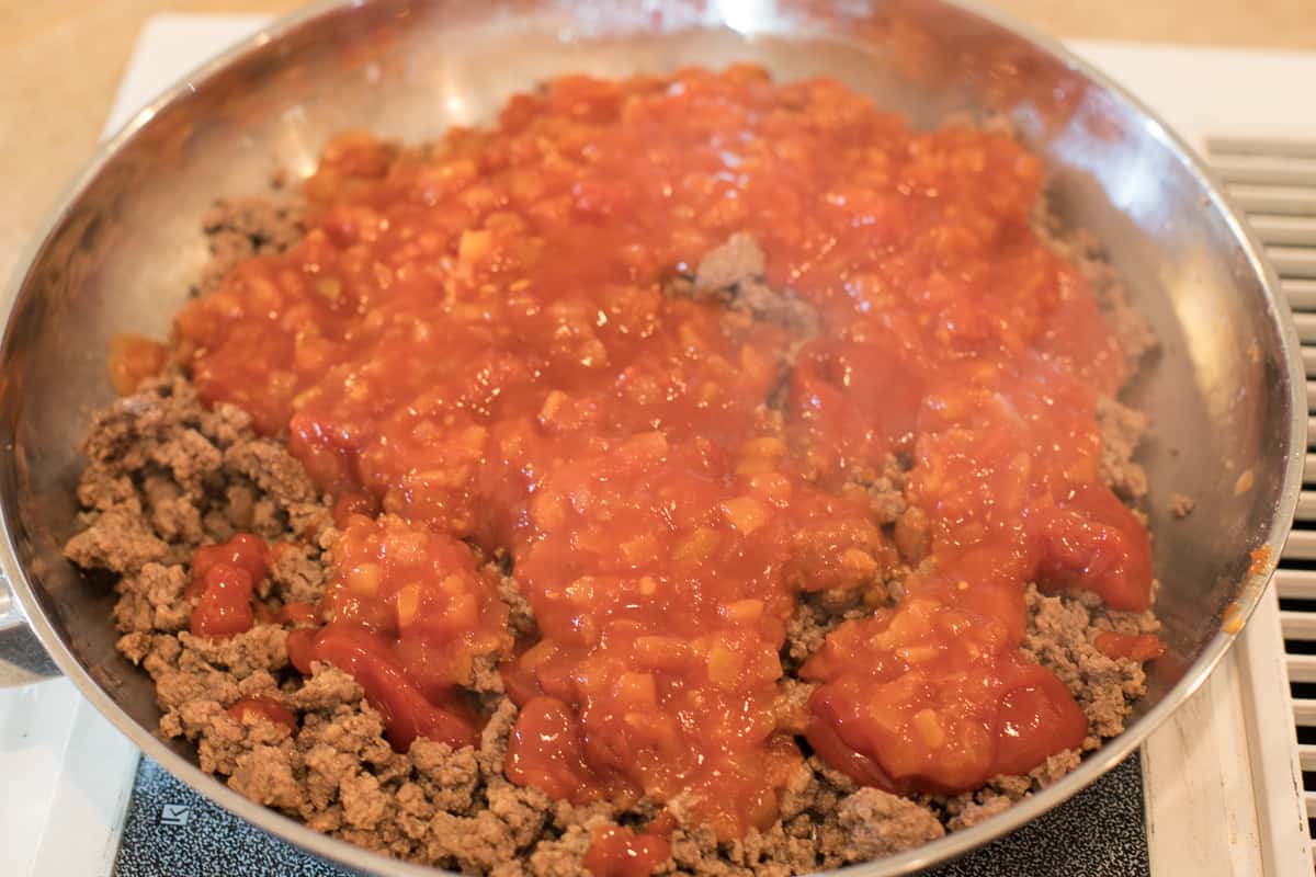 Salsa, ketchup, and cayenne pepper are added to the ground beef in the frying pan.