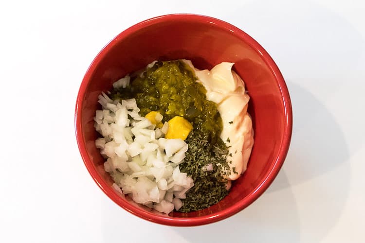 Mayonnaise, sweet relish, diced onions, yellow mustard, and parsley flakes in a bowl.