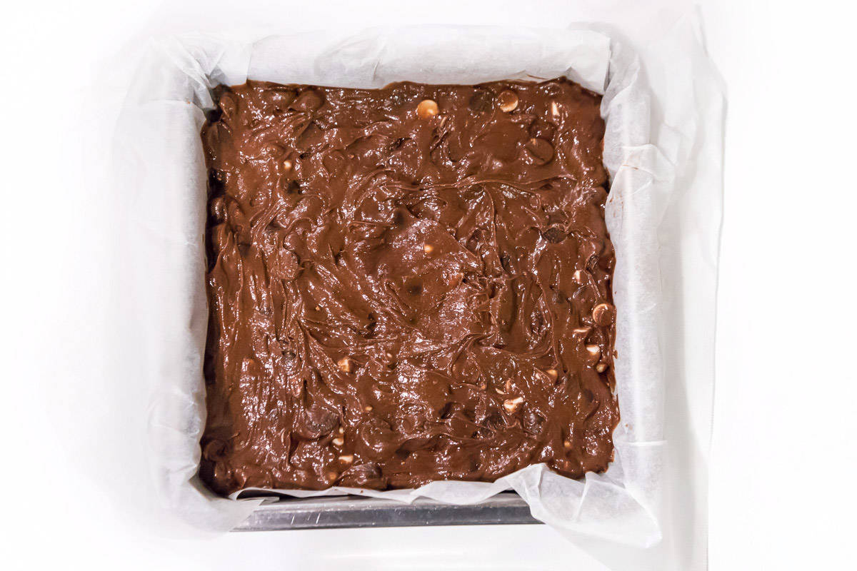 Fudgy triple chocolate brownie batter spread in a nine by nine inch baking pan.