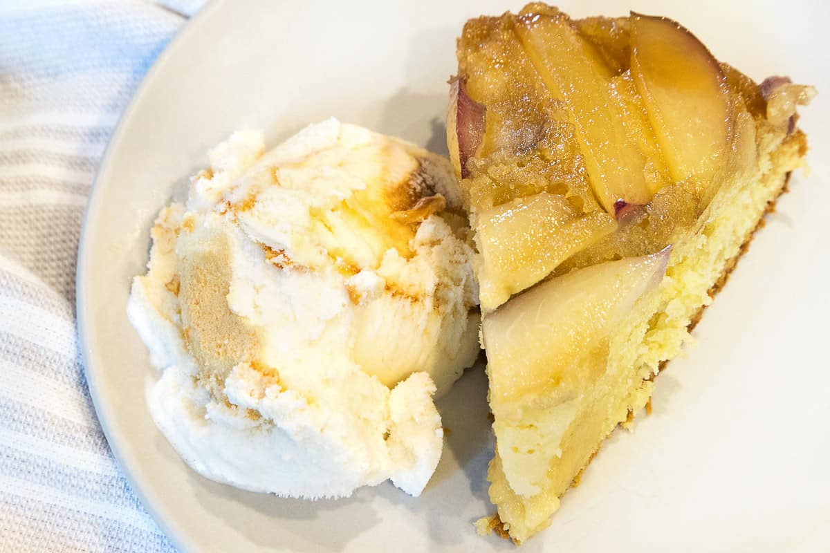 A slice of white nectarine cake (upside-down) with ice cream on a plate.